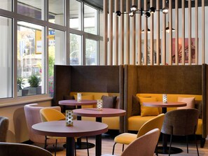 A modern interior with round tables and cushioned seating, large windows, and a decorative light fixture. - ibis Paderborn City (Paderborn)