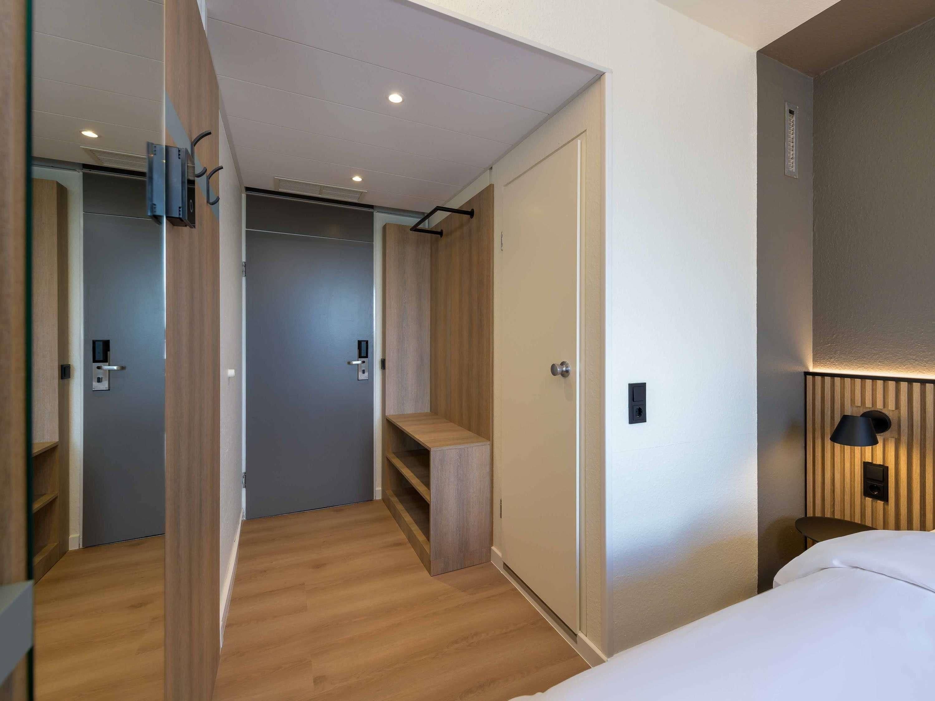 A modern hotel room with a wooden floor, a bed, a desk, and a wardrobe.
