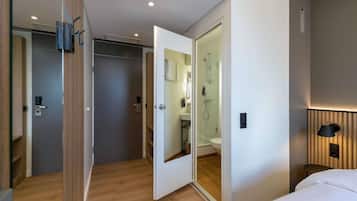 Ein Hotelzimmer mit Holzboden, einem Bett, einem Badezimmer mit Duschkabine aus Glas und einer Wandleuchte.