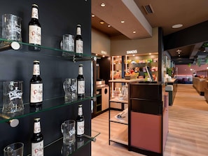 A bar area with shelves displaying bottles and glasses, a snack counter, and a seating area. - ibis Paderborn City (Paderborn)