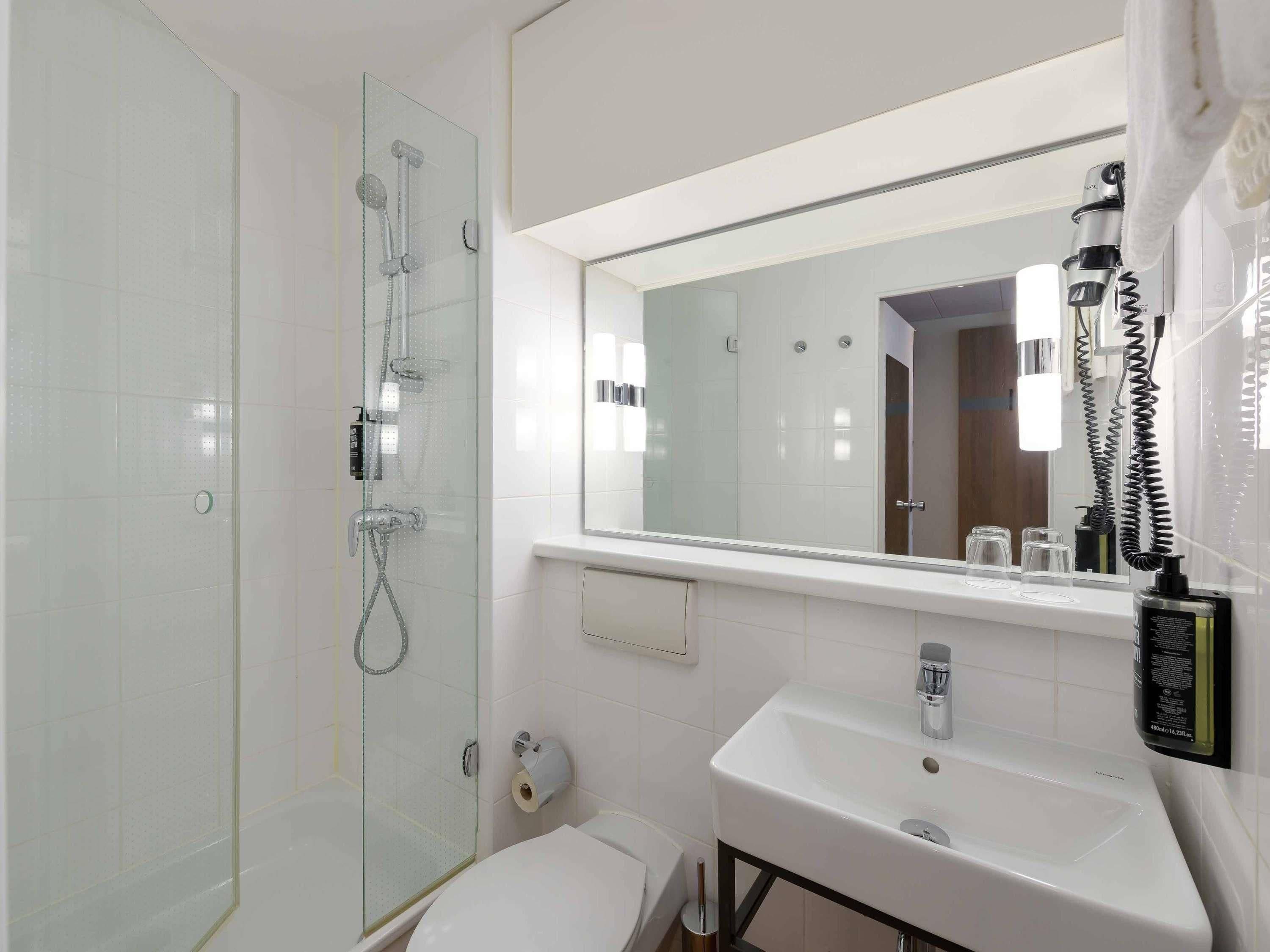 A bathroom with a glass shower enclosure, a white sink with a mirror above it, and a toilet.