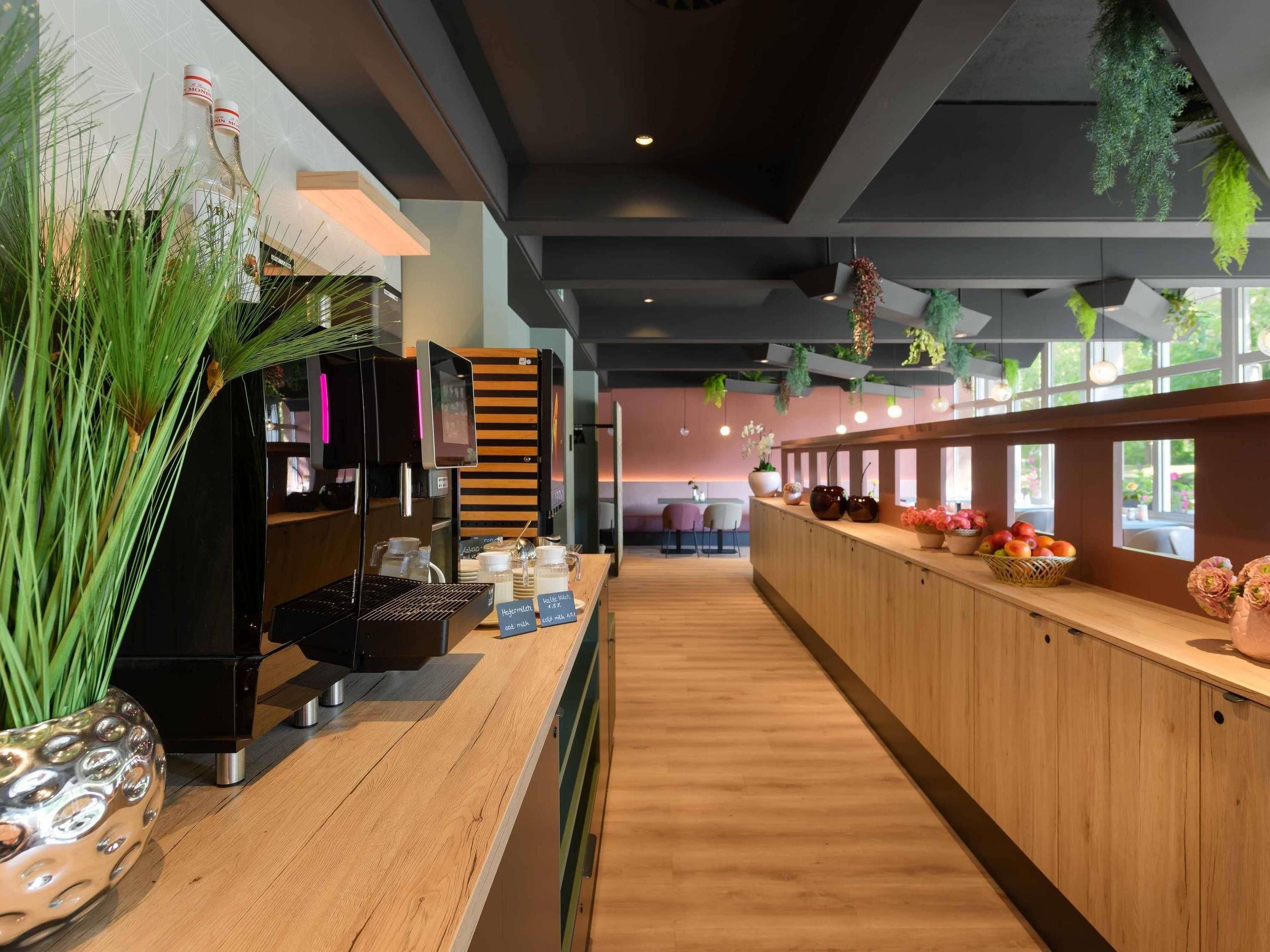 A modern bar area with a coffee machine, a wooden counter, and a seating area in the background.
