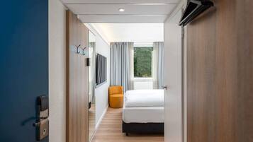 A modern hotel room with a bed, a chair, a television, and a window with curtains.
