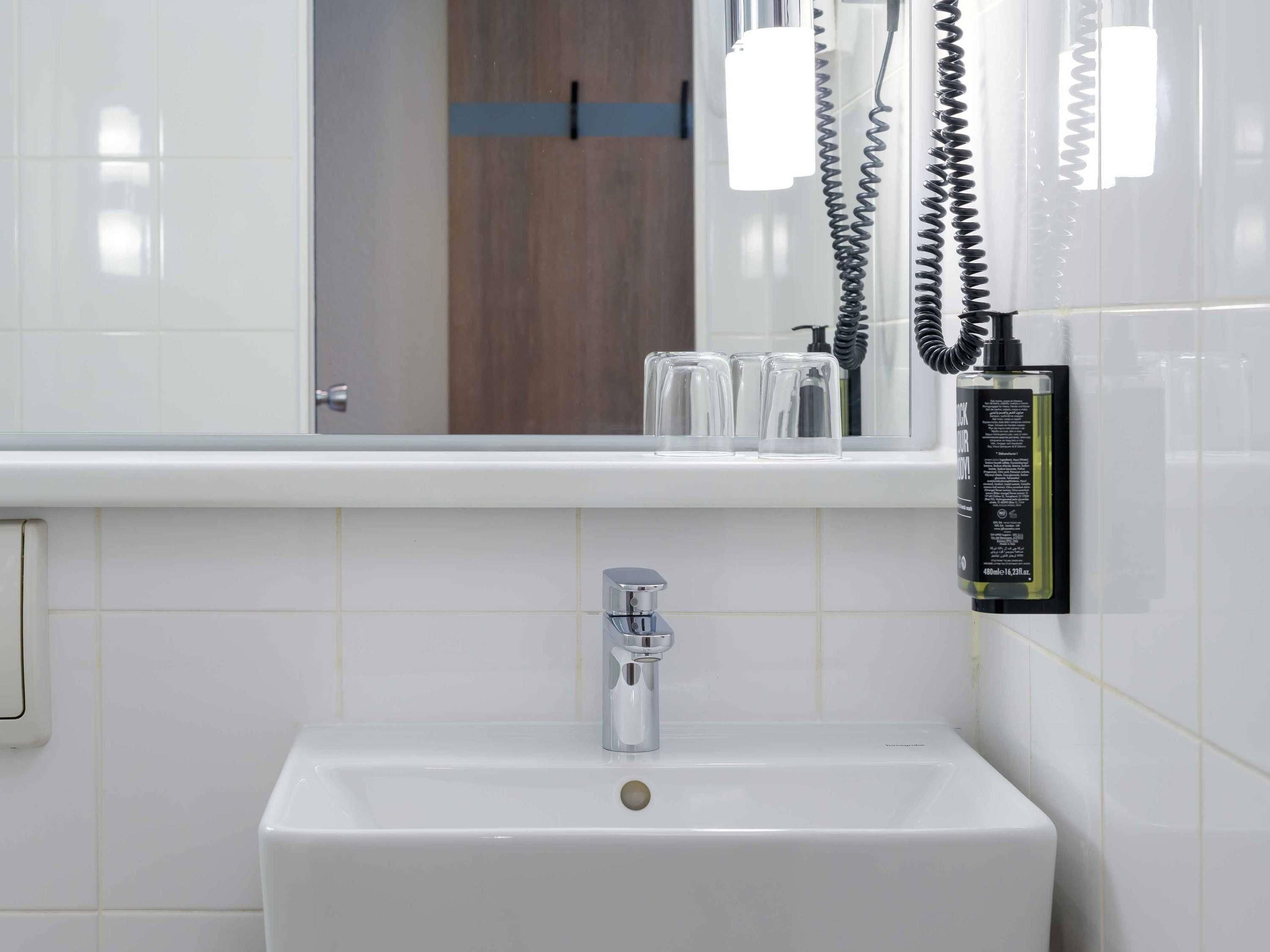 A bathroom with a white sink, a mirror, and a bottle of shampoo.