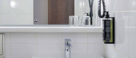 Une salle de bain avec un lavabo blanc, un miroir et une bouteille de shampoing.