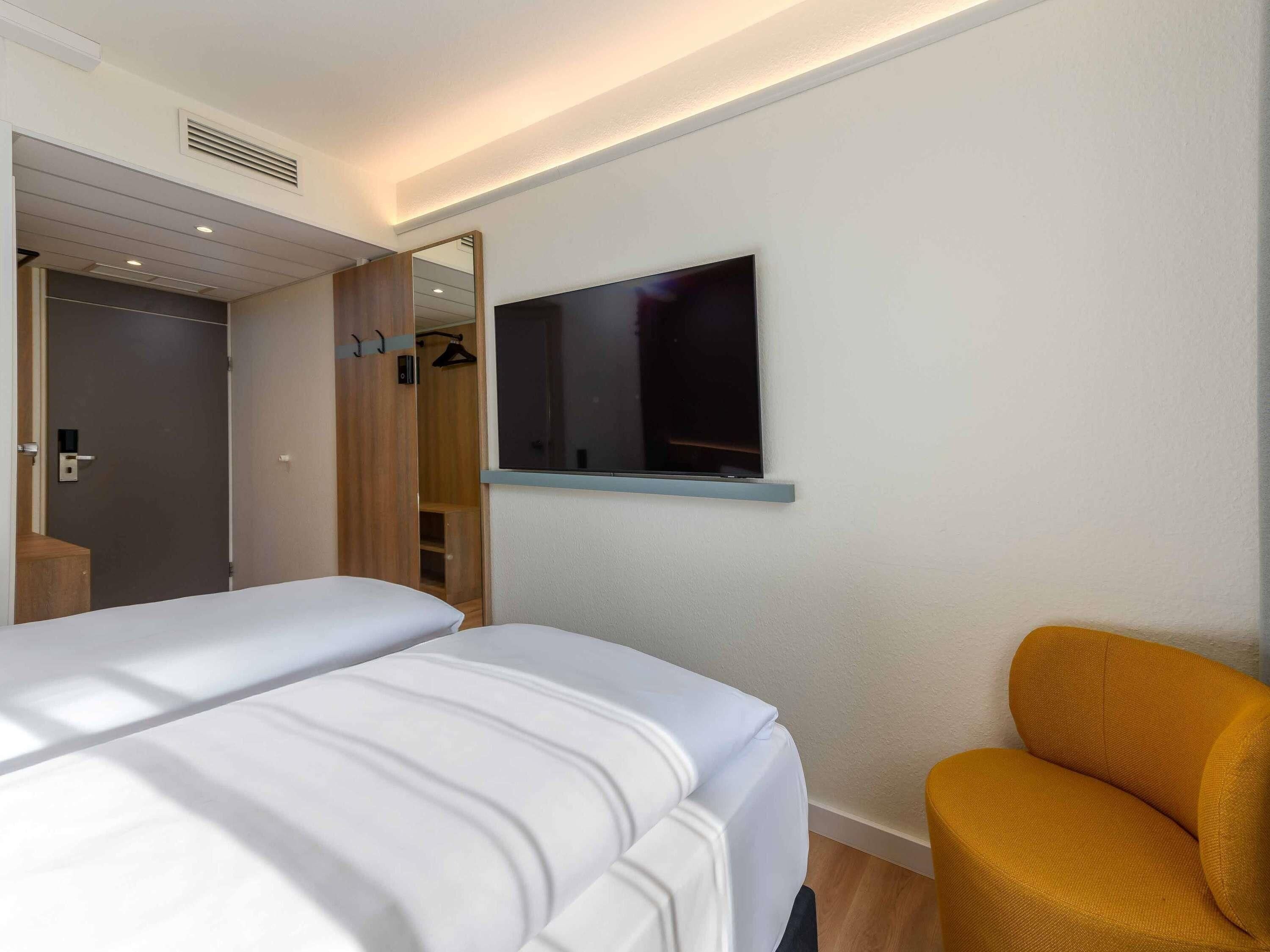 Et hotelværelse med en seng, et fjernsyn ophængt på væggen og et klædeskab.