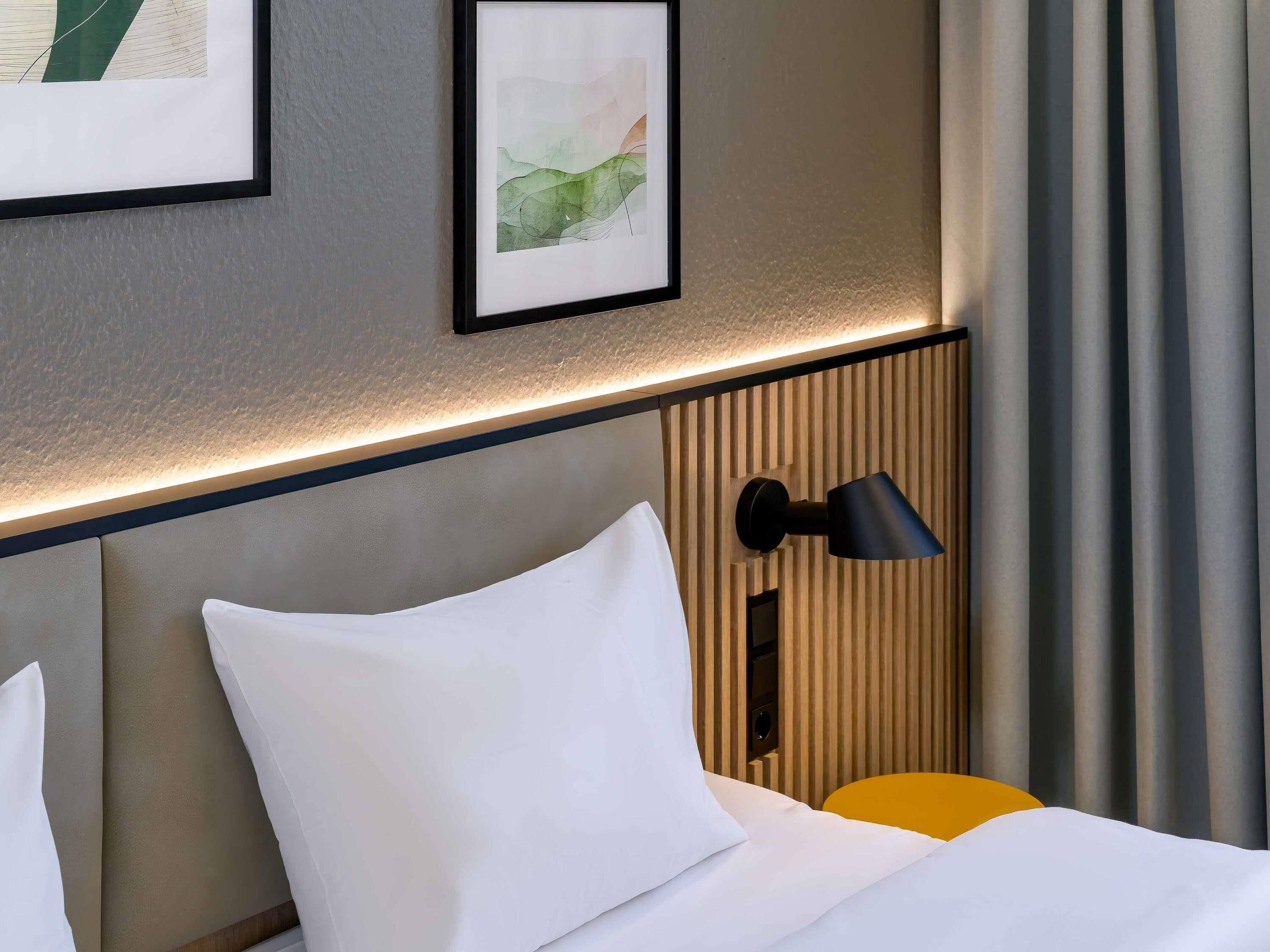 A hotel room with a bed, a bedside table, a lamp, and a framed picture on the wall.