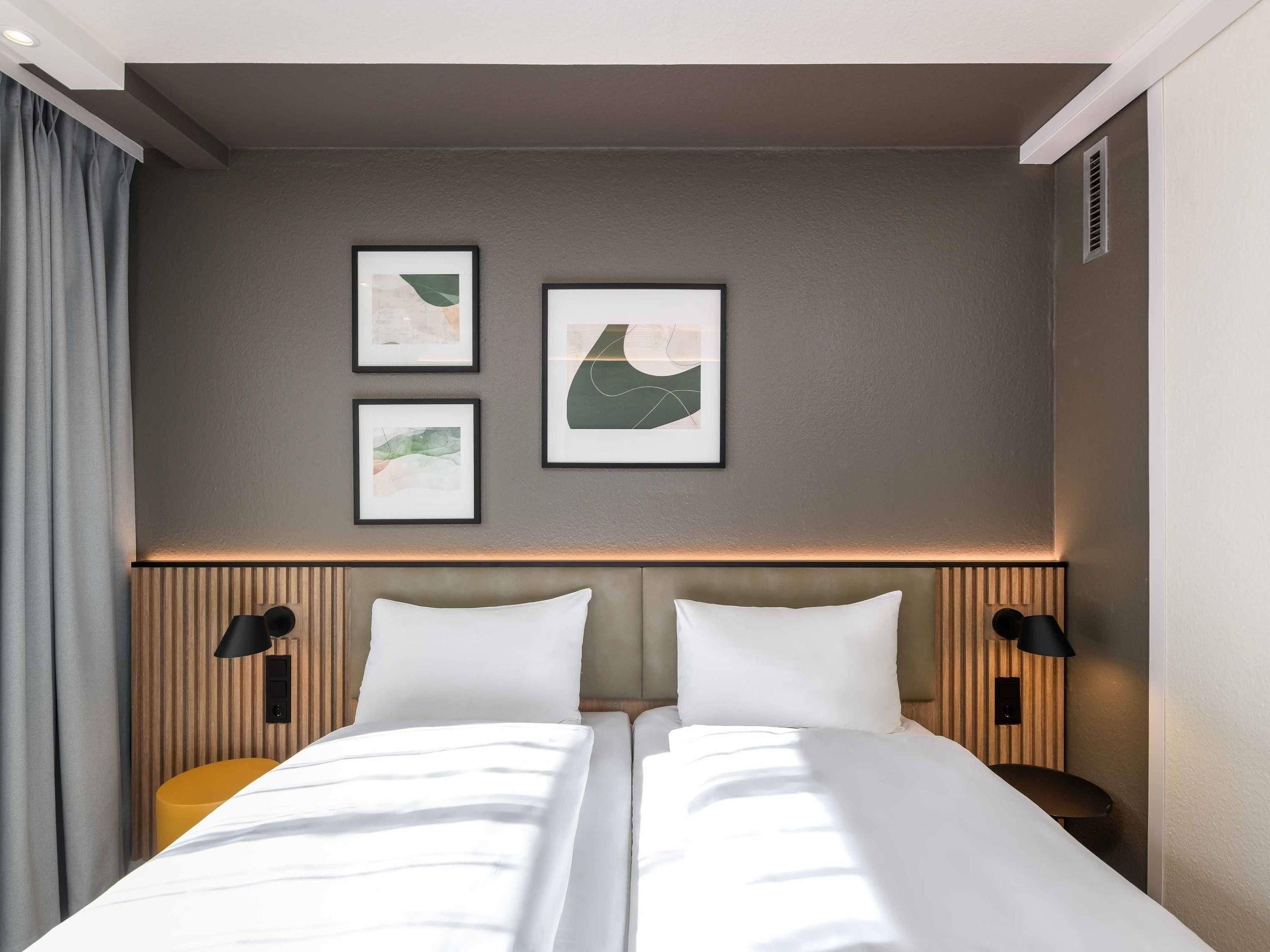 Habitación de hotel con cama doble, dos mesitas de noche, cabecera con iluminación integrada y tres cuadros enmarcados en la pared.