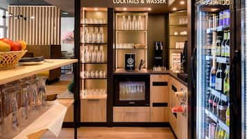 A bar area with shelves of bottles and glasses, a refrigerator stocked with beverages, and a counter with a coffee machine.