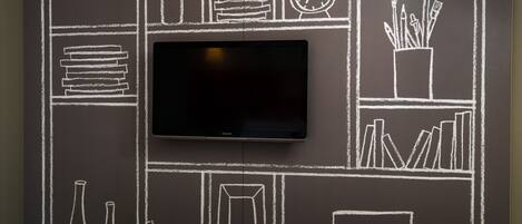 A wall with a flat-screen TV mounted above a chalkboard with various drawings.