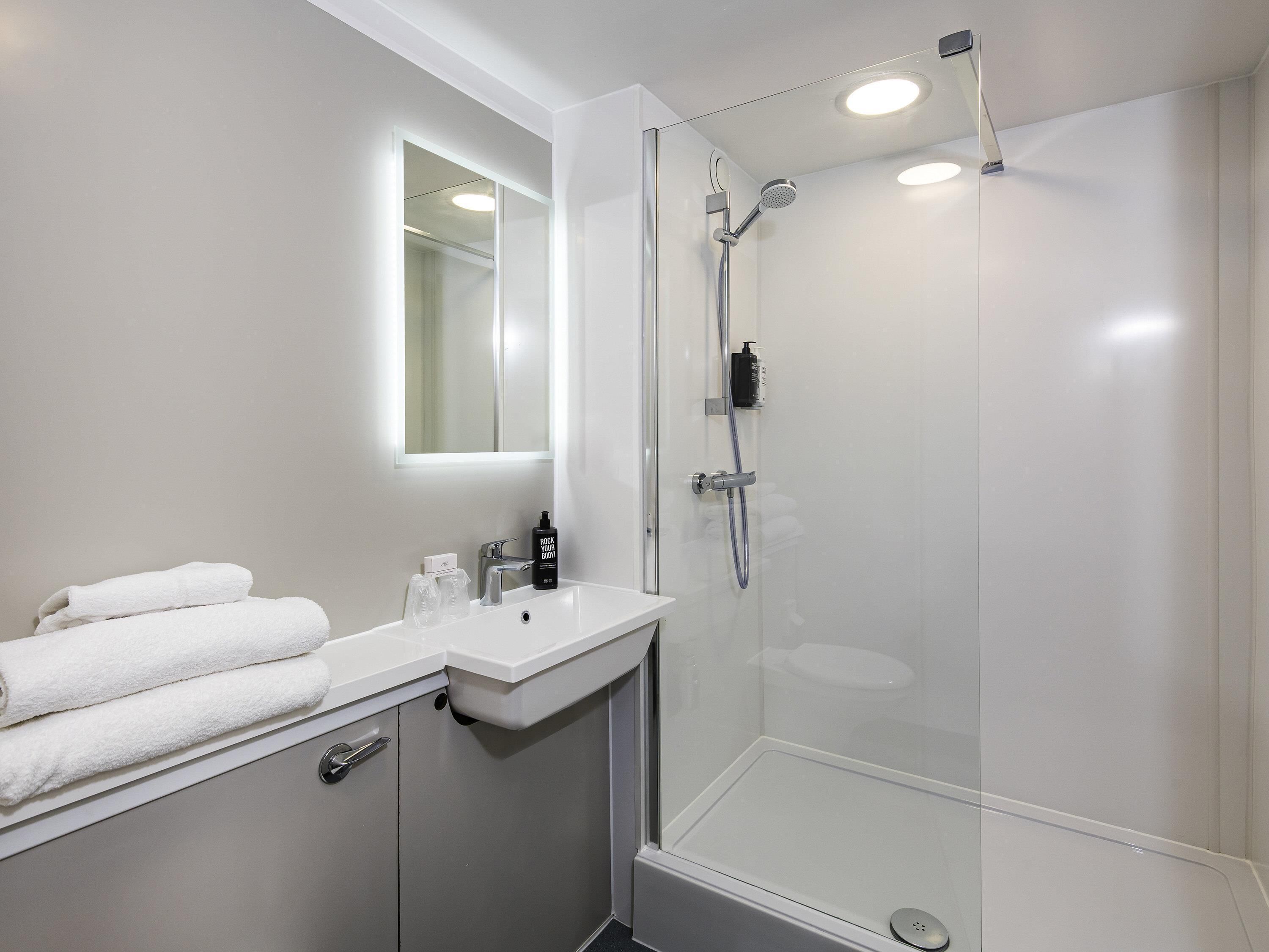 Un baño moderno con ducha acristalada, un lavabo blanco y un espejo encima.