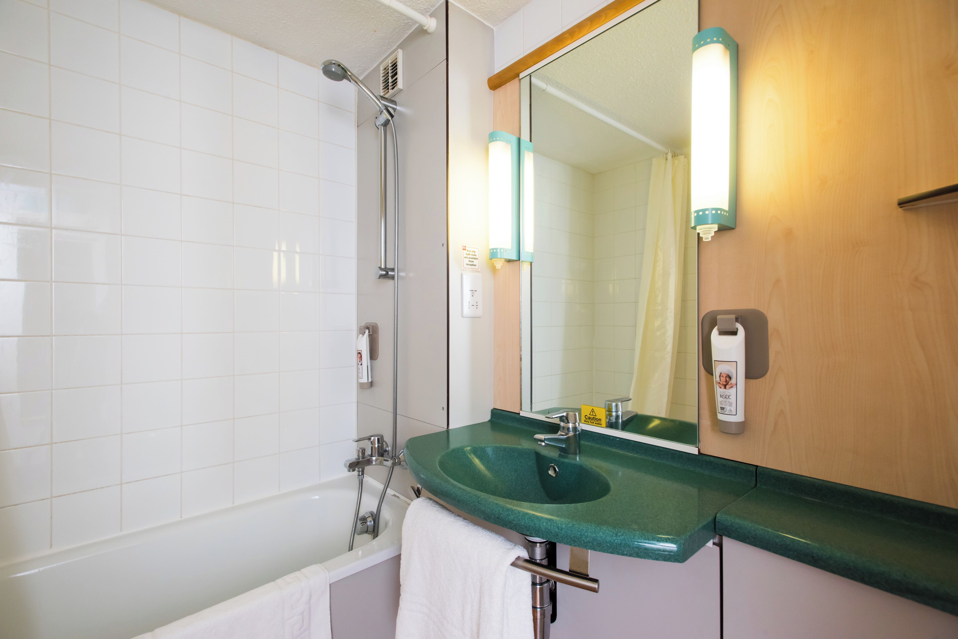 Een badkamer met een groene wastafel, een spiegel, een handdoekhouder en een douche.