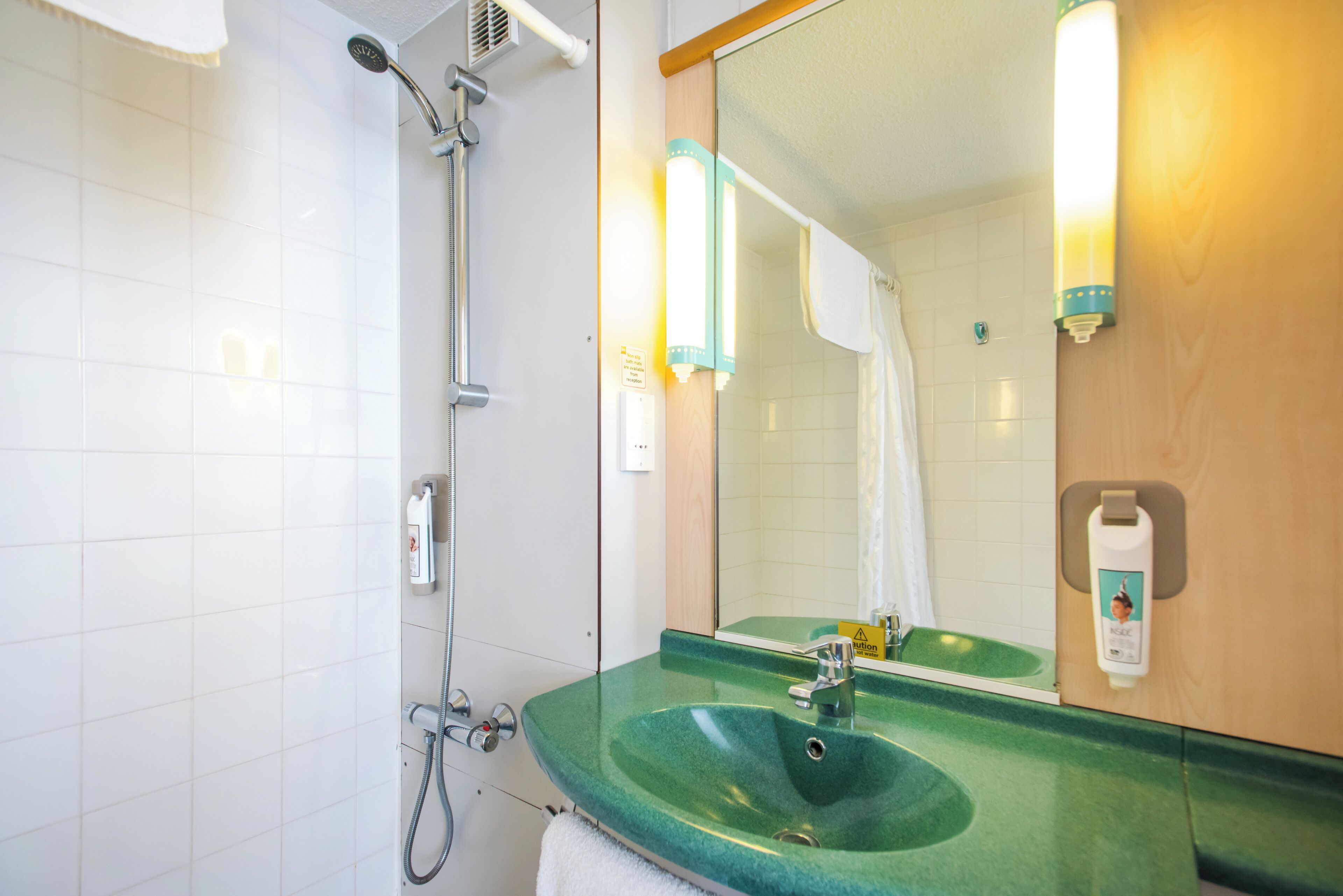 Une salle de bain avec un lavabo vert, une douche, un miroir et un porte-serviettes.