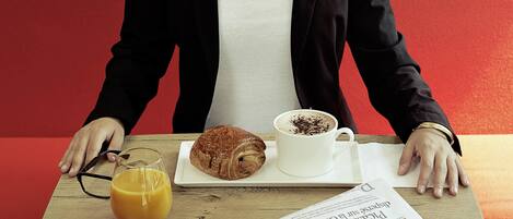 A person seated at a table with a croissant, a cup of coffee, and a glass of orange juice.