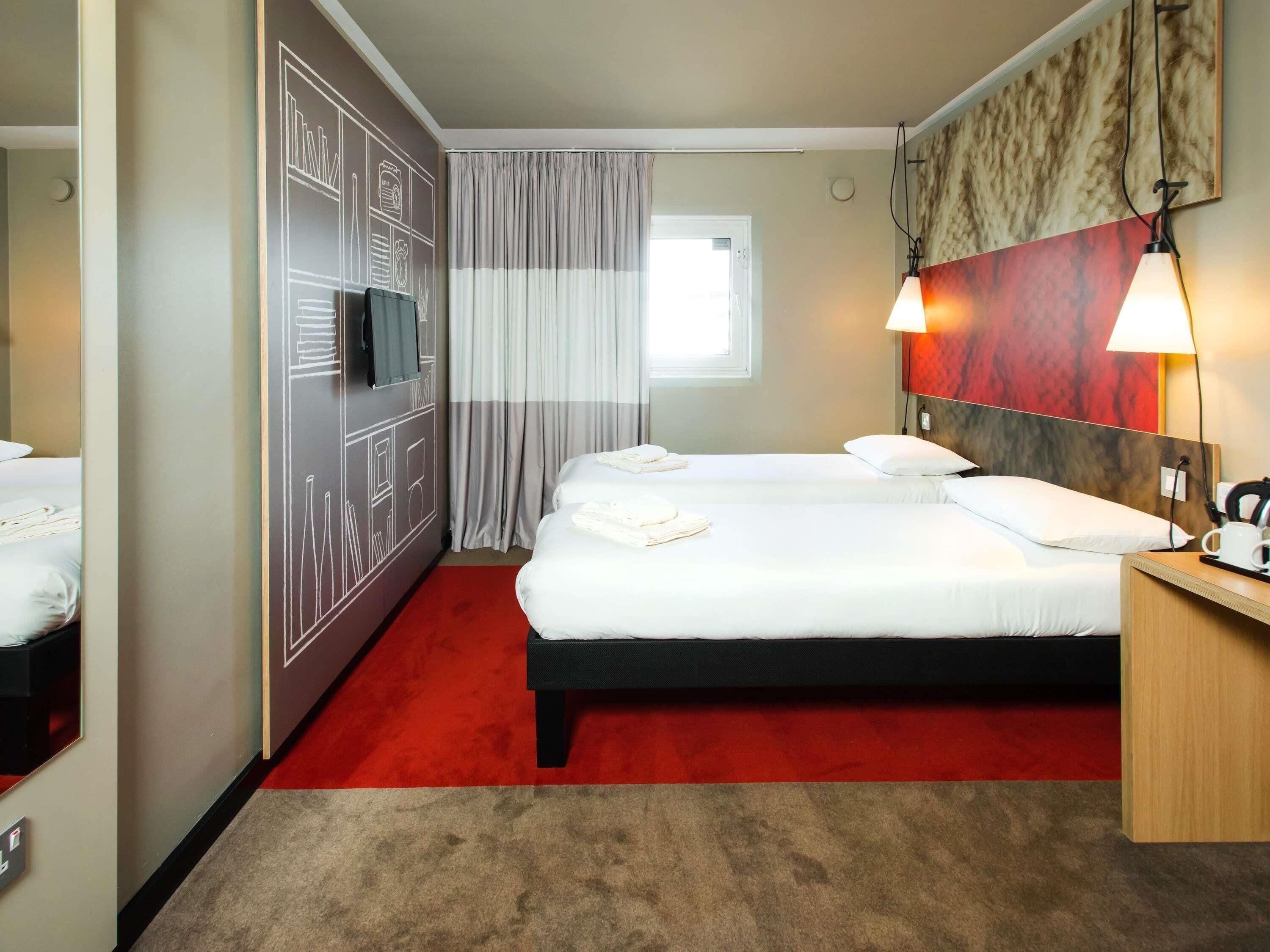 A hotel room with a large bed, a TV on the wall, a red carpet, and a wooden headboard.