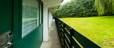 A corridor with a green exterior wall, a black railing, and a view of a grassy area with trees.