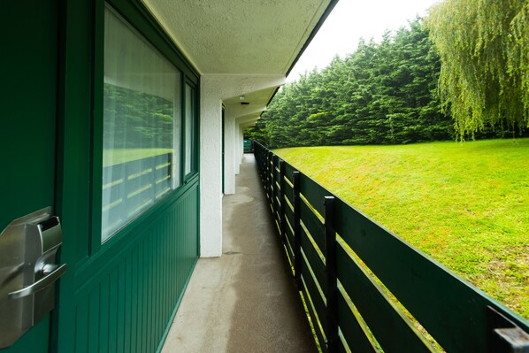 A corridor with a green exterior wall, a black railing, and a view of a grassy area with trees. - ibis Plymouth (Plymouth)