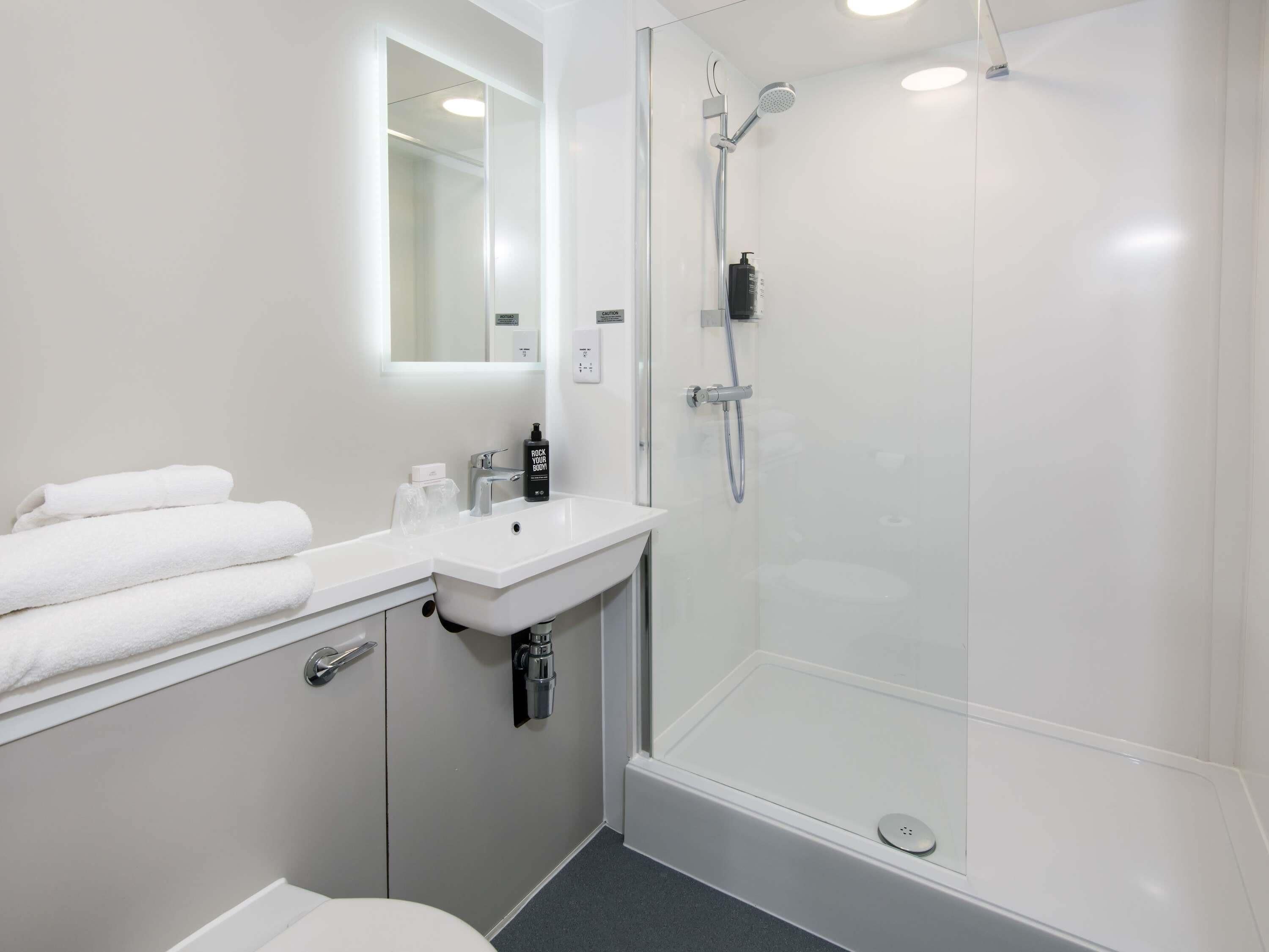 Une salle de bain moderne avec une douche à parois de verre, un lavabo blanc et un miroir au-dessus du lavabo.