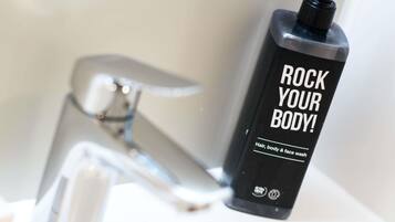 Een zwarte fles met een pompdispenser waarop staat 'ROCK YOUR BODY!' naast een chromen kraan.