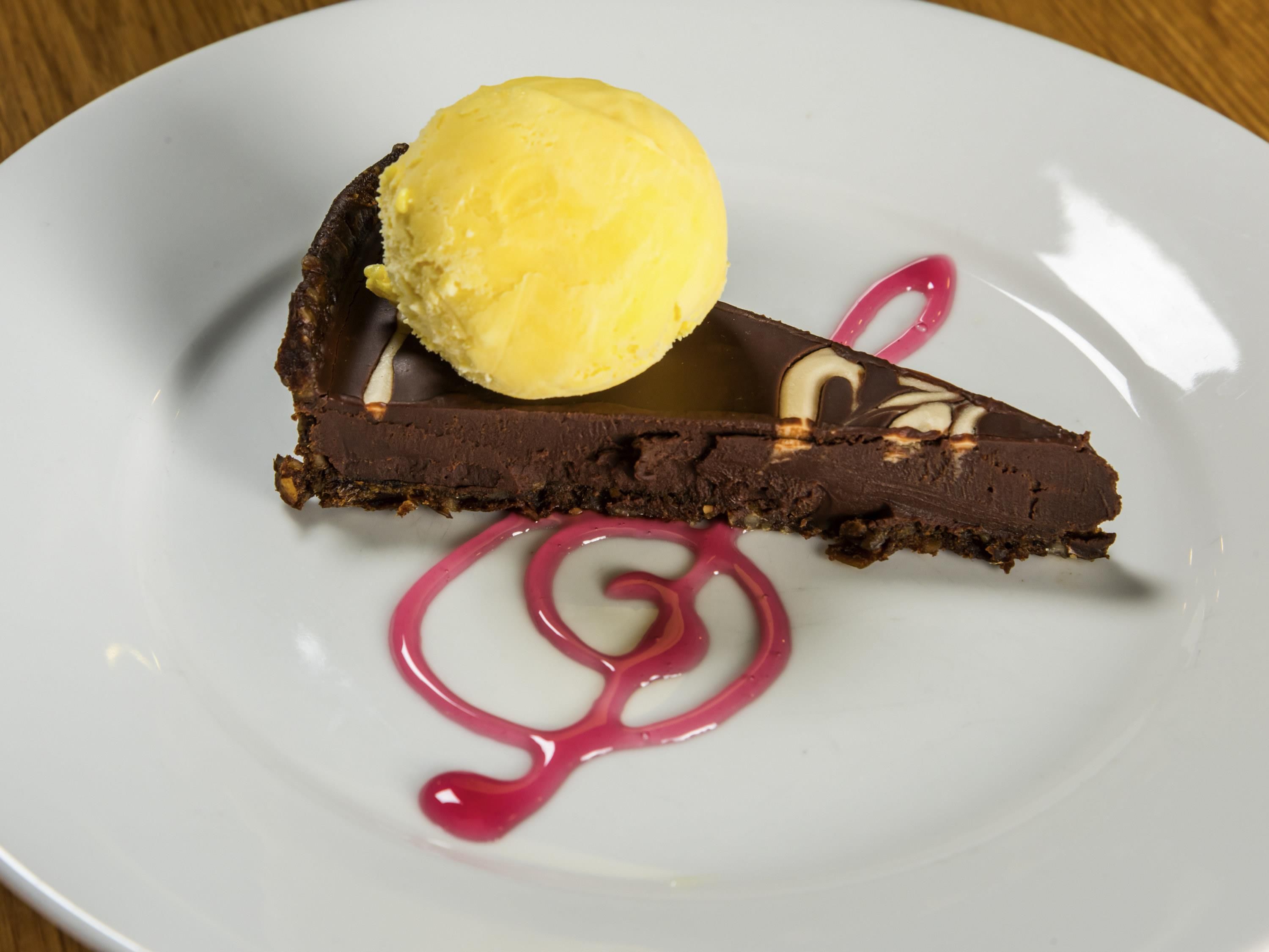 Un plato de postre con una tarta de chocolate, una bola de helado de vainilla y salsa rosa.