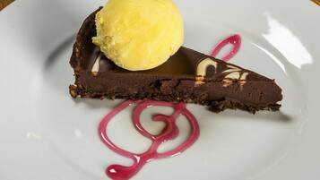 Un plato de postre con una tarta de chocolate, una bola de helado de vainilla y salsa rosa.