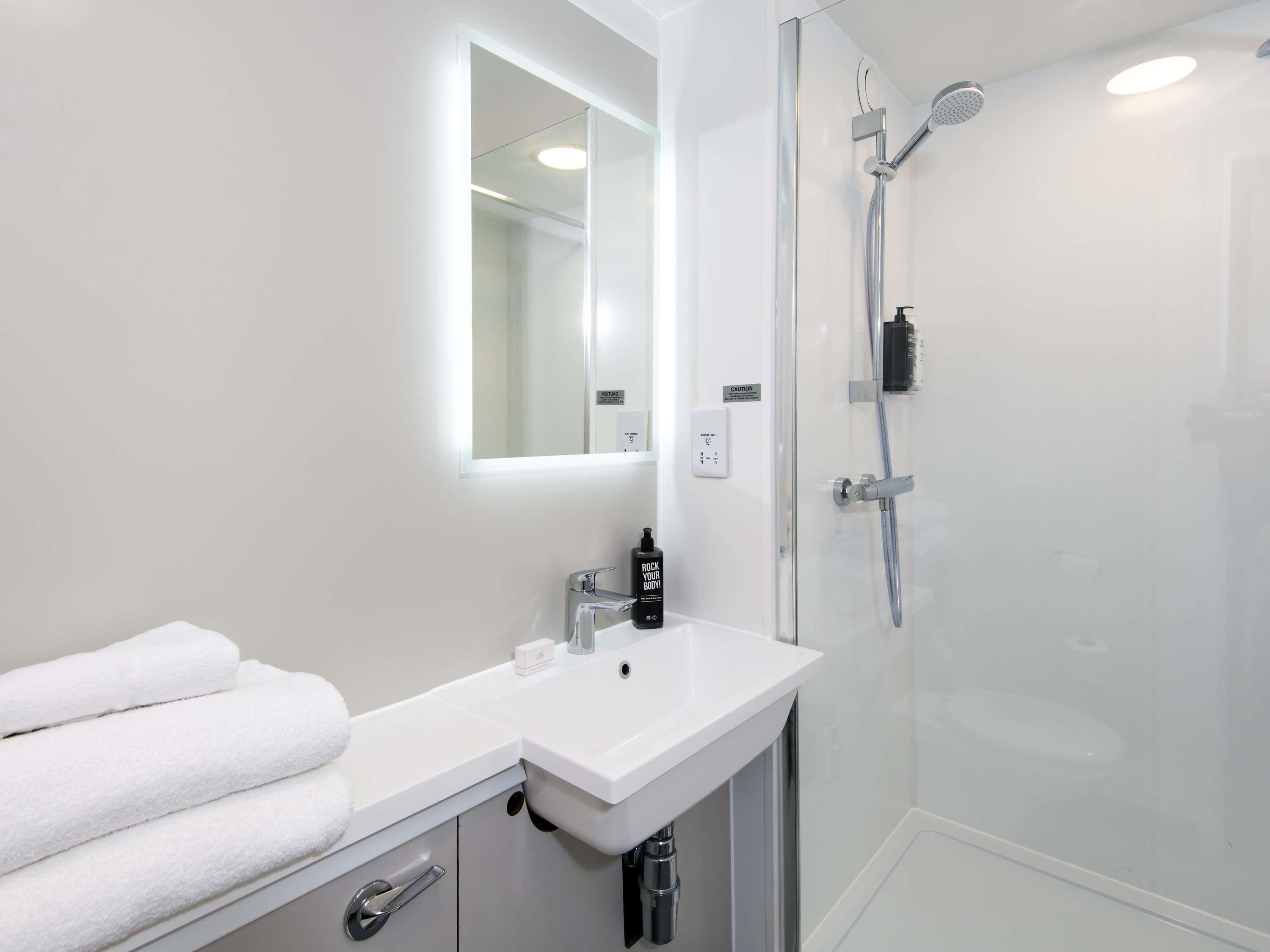 Un baño moderno con lavabo blanco, espejo y cabina de ducha de vidrio.