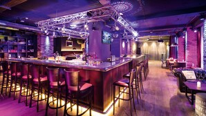 A bar area with a long counter, multiple bar stools, and a brick wall backdrop. - Hotel PULSE8 (Prague)