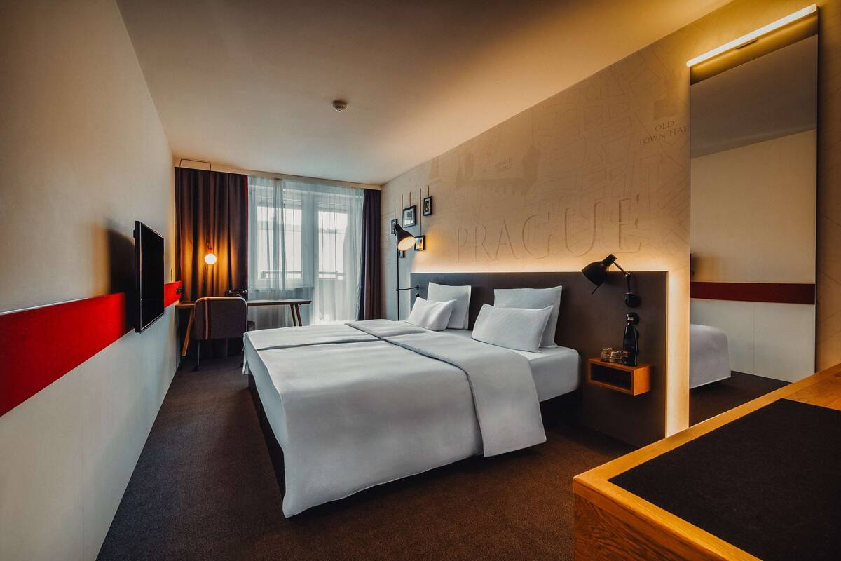 Habitación de hotel con una cama grande, un escritorio, una silla, un televisor y un espejo.