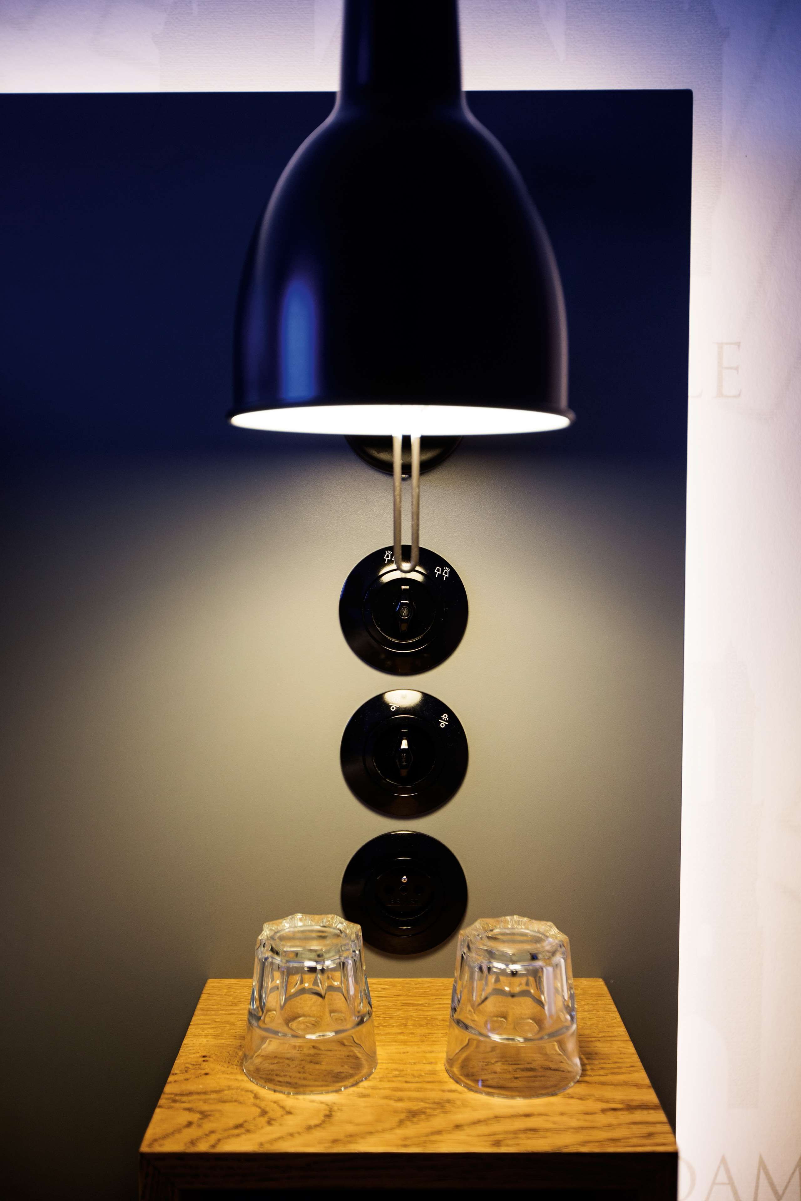 Una lámpara moderna con pantalla negra y tres elementos esféricos sobre una mesa de madera.