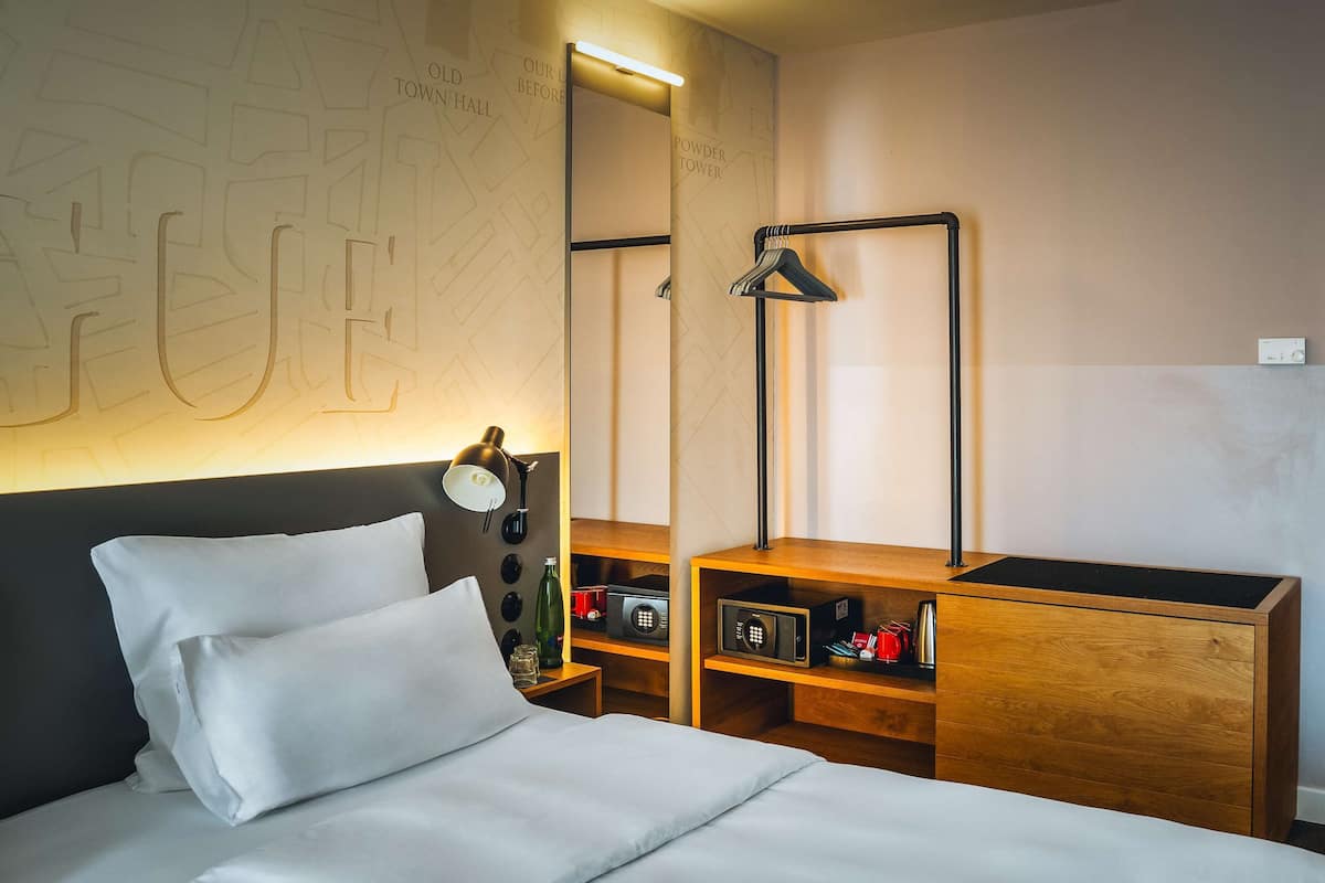 Habitación de hotel ordenada con cama, mesitas de noche, espejo y armario.