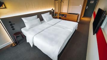 A neatly made bed with white linens, a bedside table with a lamp, and a small stool.