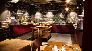 A cozy cafe with wooden tables and chairs, a chalkboard wall with food-related drawings, and a variety of pastries displayed. - Hotel PULSE8 (Prague)