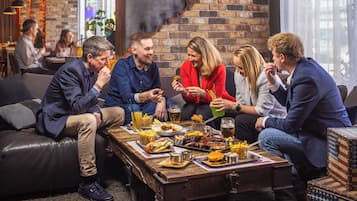 A group of people dining at a rustic wooden table with various dishes and drinks, in a cozy indoor setting with brick walls and leather seating.