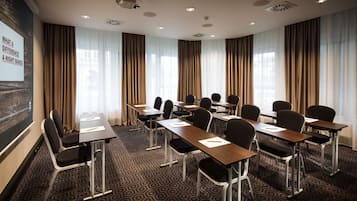 Ein Konferenzraum mit Projektionsleinwand, mehreren Tischen und Stühlen für Besprechungen.
