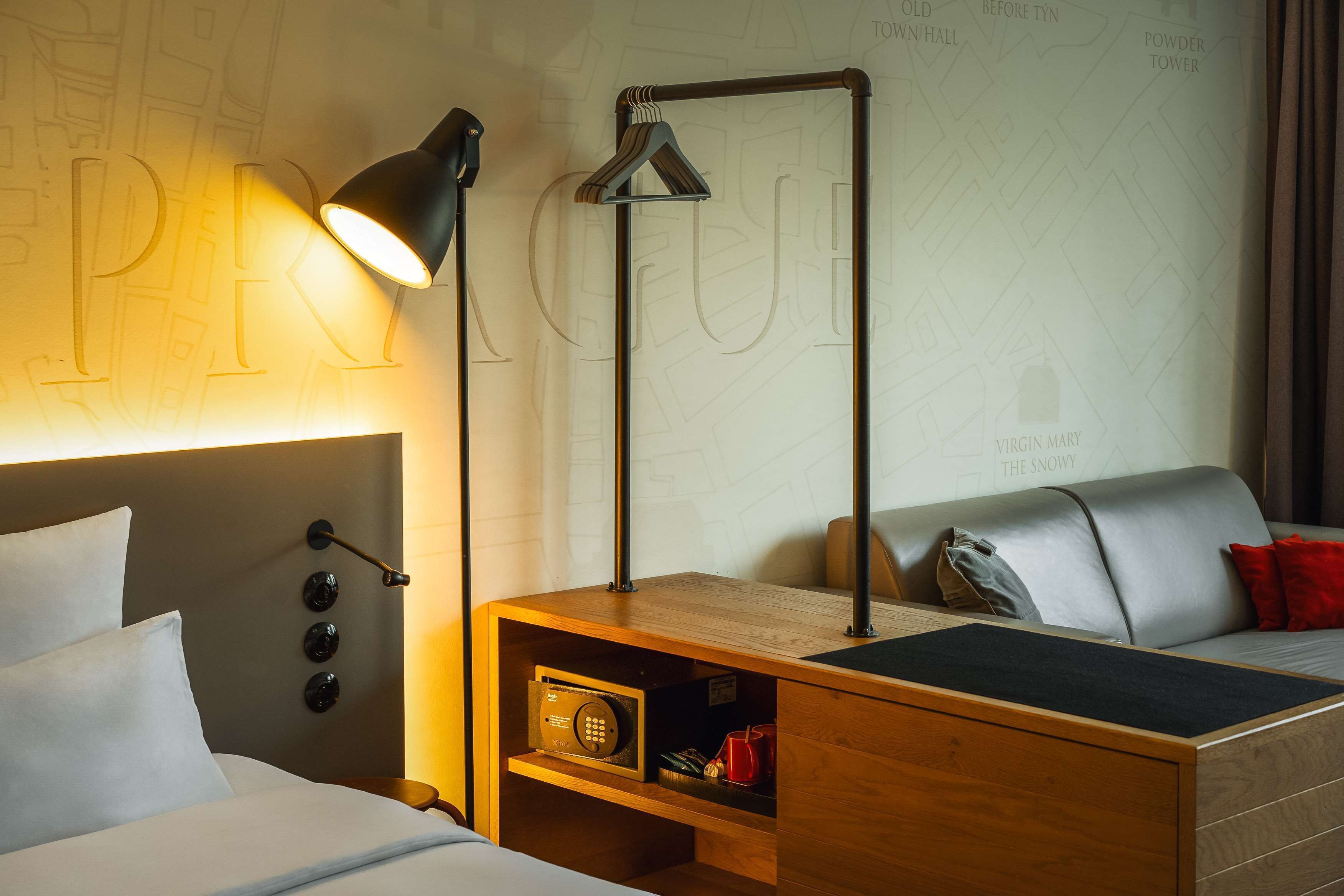 Ein Hotelzimmer mit einem Bett, einem Nachttisch mit Lampe, einem Holzbeistelltisch und einer Wand mit einer Weltkarte.