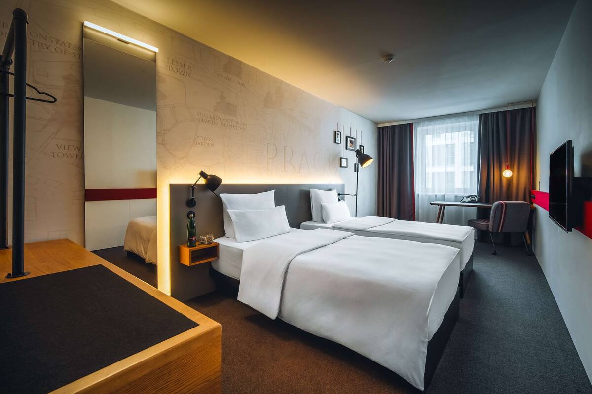 Habitación de hotel con dos camas, un escritorio, una silla, un televisor y un mapa en la pared.