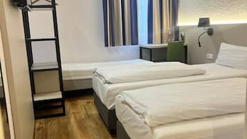 Habitación de hotel con dos camas, un escritorio, una silla, un estante y una ventana con cortinas.