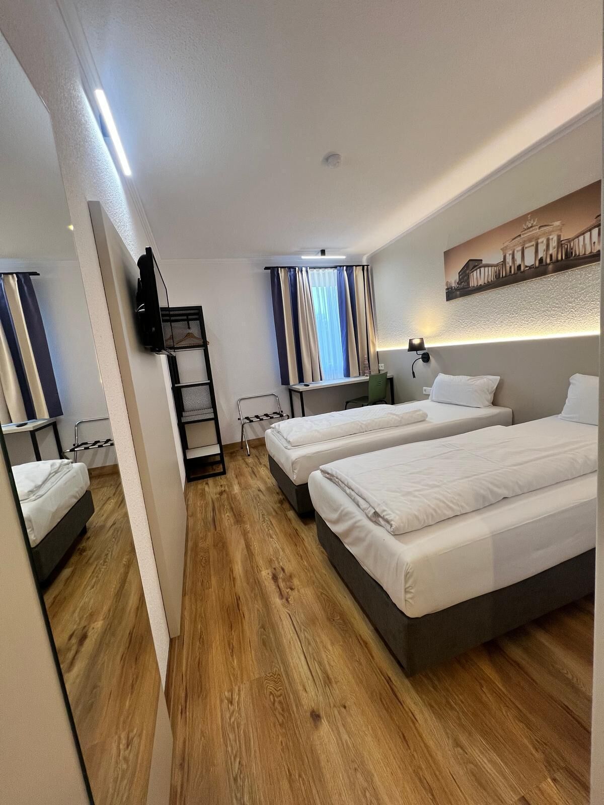 A hotel room with two beds, a desk, a chair, a TV, and a window with curtains.