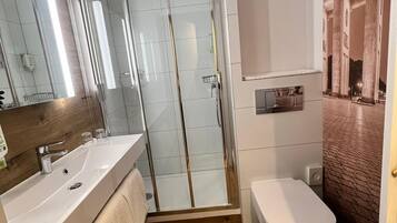 Ein modernes Badezimmer mit einer gläsernen Duschkabine, einem Waschbecken mit Spiegel und einer Toilette.