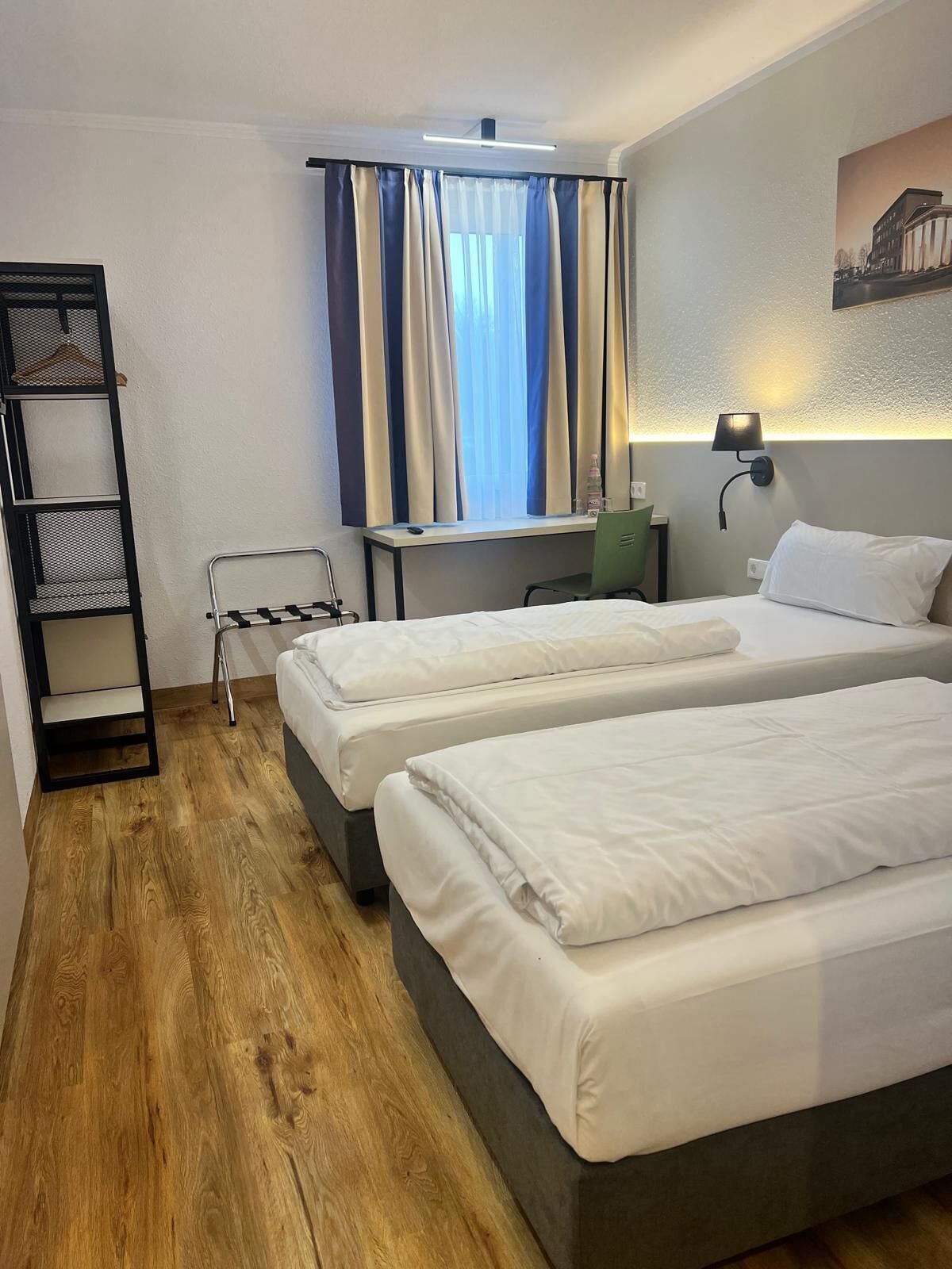 Ein Hotelzimmer mit zwei Betten, einem Schreibtisch, einem Stuhl, einem Kleiderschrank und einem Fenster mit Vorhängen.