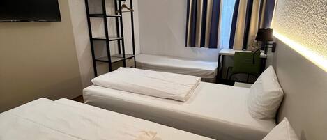 Una habitación con dos camas, un televisor montado en la pared, una mesita y una ventana con cortinas.