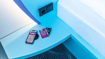 A blue corner of a room with a smartphone, a card, and a small black object on a surface.