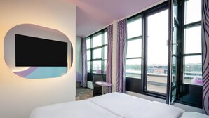 A hotel room with a bed, a TV mounted on the wall, a small table, and a chair.