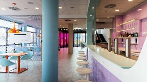 A modern bar area with a curved counter and stools, a seating area with tables and chairs, and a vibrant interior design with purple and blue tones.