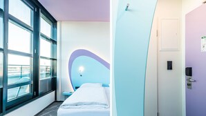 A modern hotel room with a large window, a bed, and a door with a light switch and a lock.