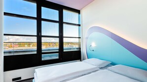 A hotel room with two beds, a large window with a view of a cityscape, and a modern wall design.
