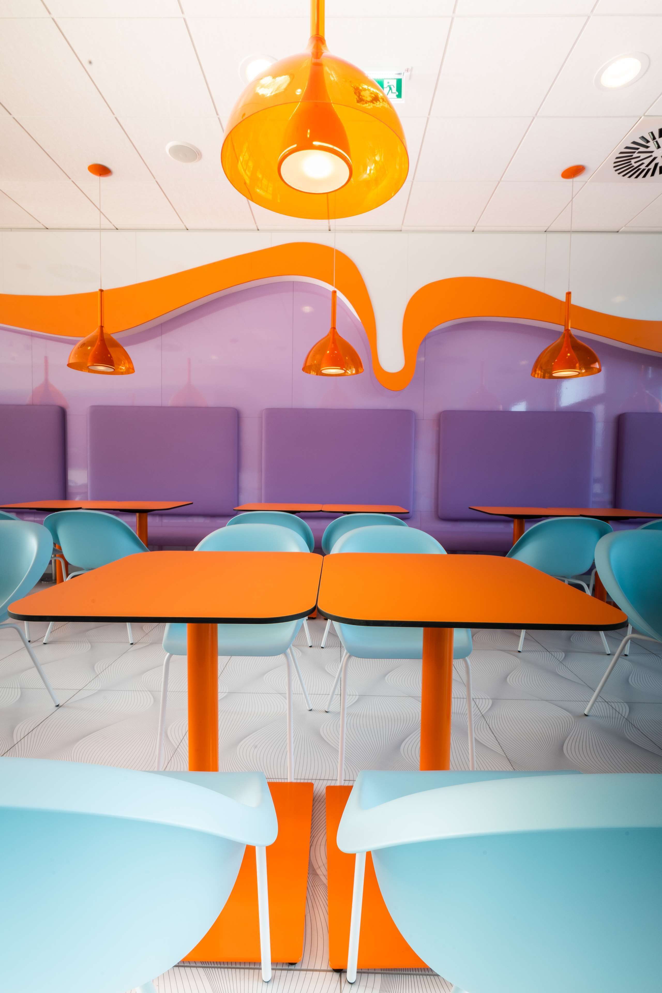 A modern interior with orange and blue seating, pendant lighting, and a patterned ceiling.