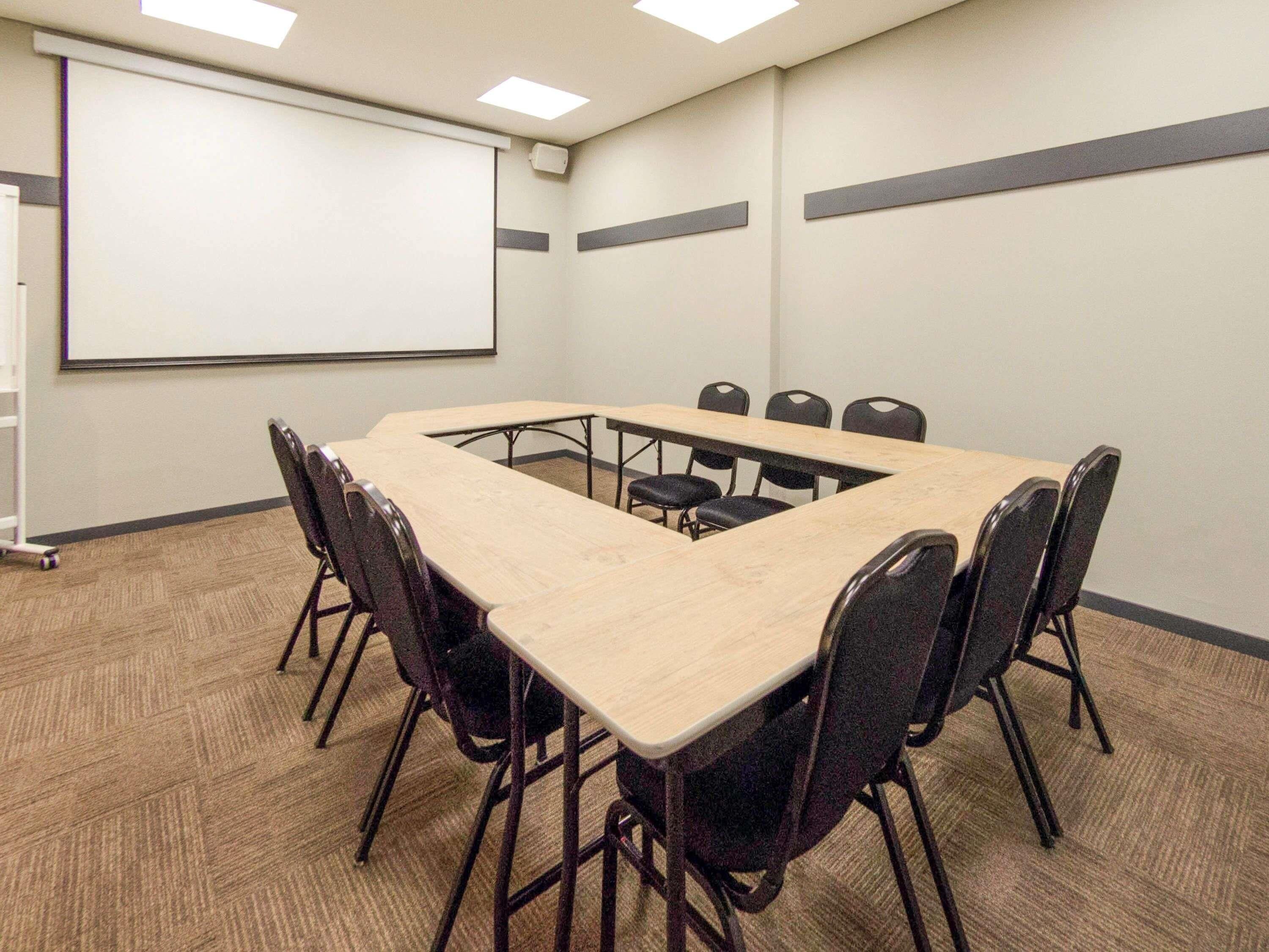 Ein Konferenzraum mit einem langen Tisch, sechs Stühlen, einer Projektionsleinwand und einem Teppichboden.
