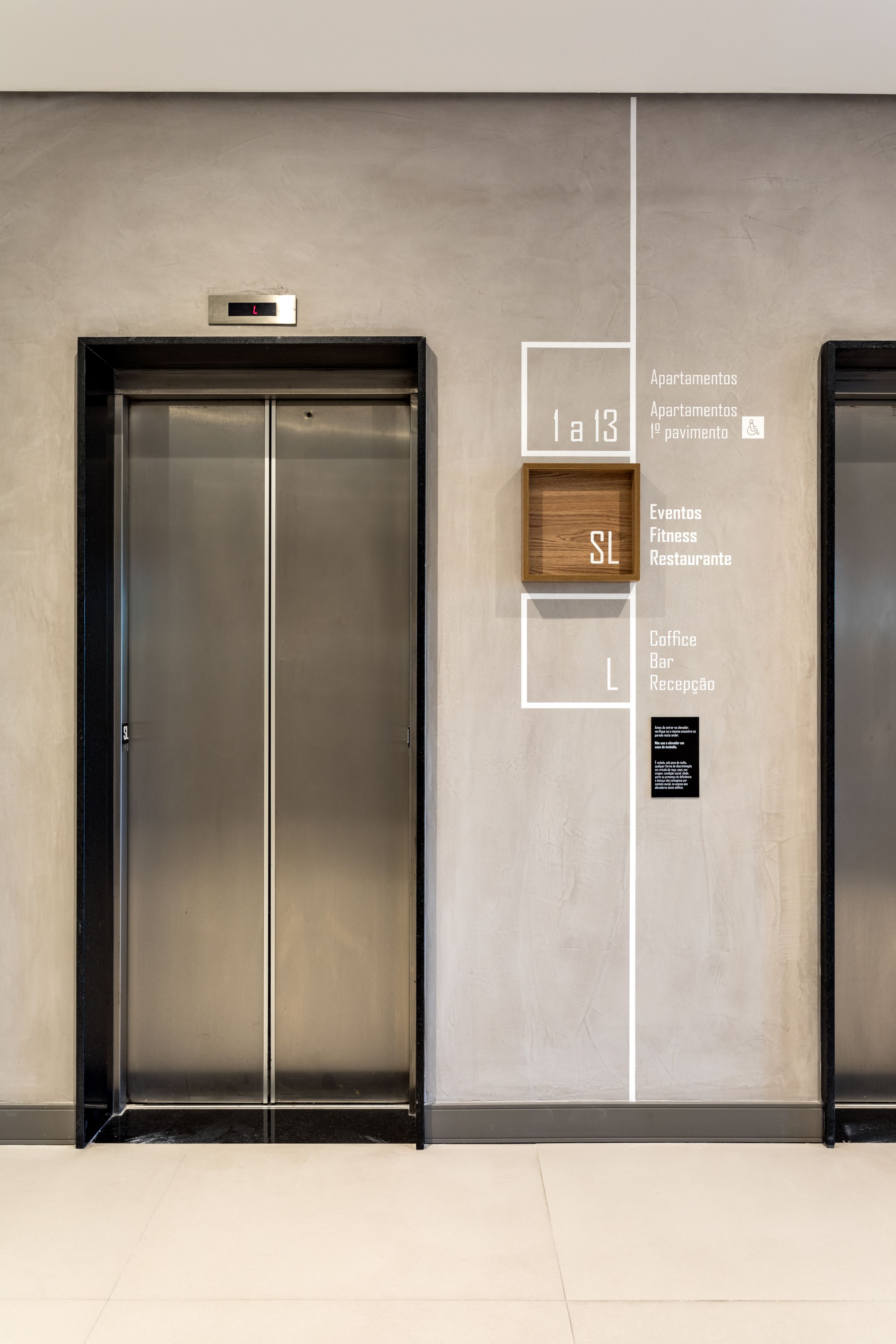 A modern elevator with a digital display, flanked by a wall with directional signs indicating amenities like apartments, fitness, and a restaurant.