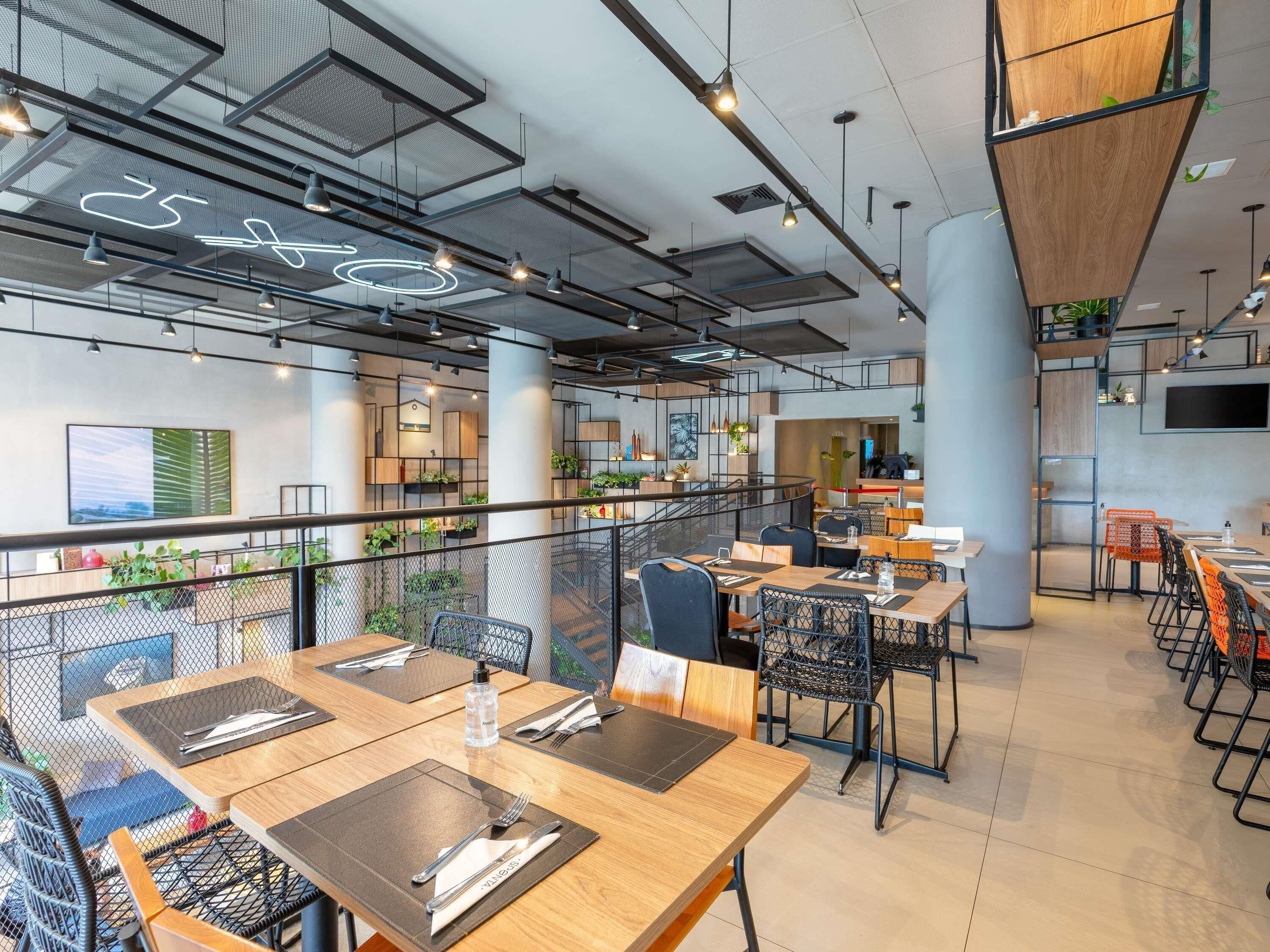 A modern dining area with tables, chairs, and a mezzanine level with plants.
